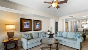 A living room with two light blue sofas, a round coffee table, a wooden side table, a floor lamp, and two framed pictures on the wall.