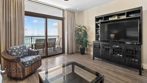 Ein Wohnzimmer mit einem großen Fernseher, einem Korbsessel, einem Glastisch und einem Balkon mit Blick.