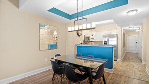 Eine moderne Küche mit blauer Akzentwand, einem Glastisch mit Stühlen und einer sichtbaren Kochinsel mit Spüle.