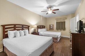 Habitación de hotel con dos camas, ventilador de techo, televisor y cómoda.