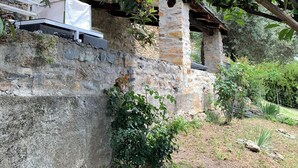 Een stenen muur met een kleine tuin, een witte structuur erboven en uitzicht op de omliggende groene omgeving.