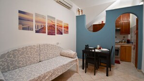 A living room with a sofa, a dining table with chairs, and a kitchen area visible through an archway.