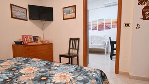 A bedroom with a bed, a wooden dresser, a chair, and a TV mounted on the wall.