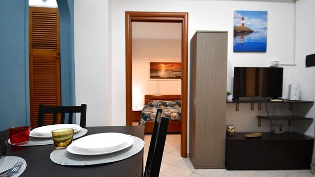 A dining area with a table set for two, a television, and a painting on the wall.