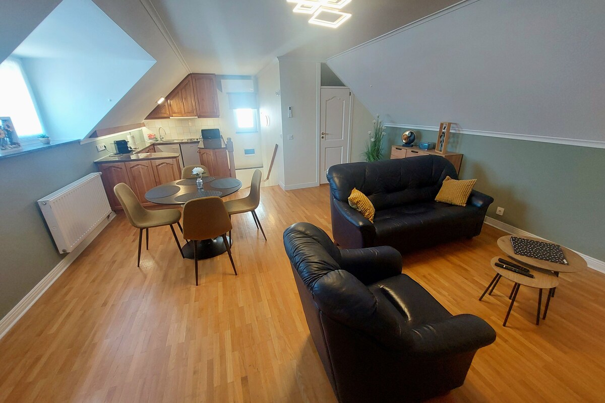 Un espace de vie compact comprenant un coin repas, un canapé en cuir noir et une petite table d’appoint.