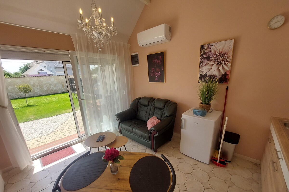 Un salon avec un canapé, une petite table sur laquelle est posé un vase, un réfrigérateur et une plante en pot.