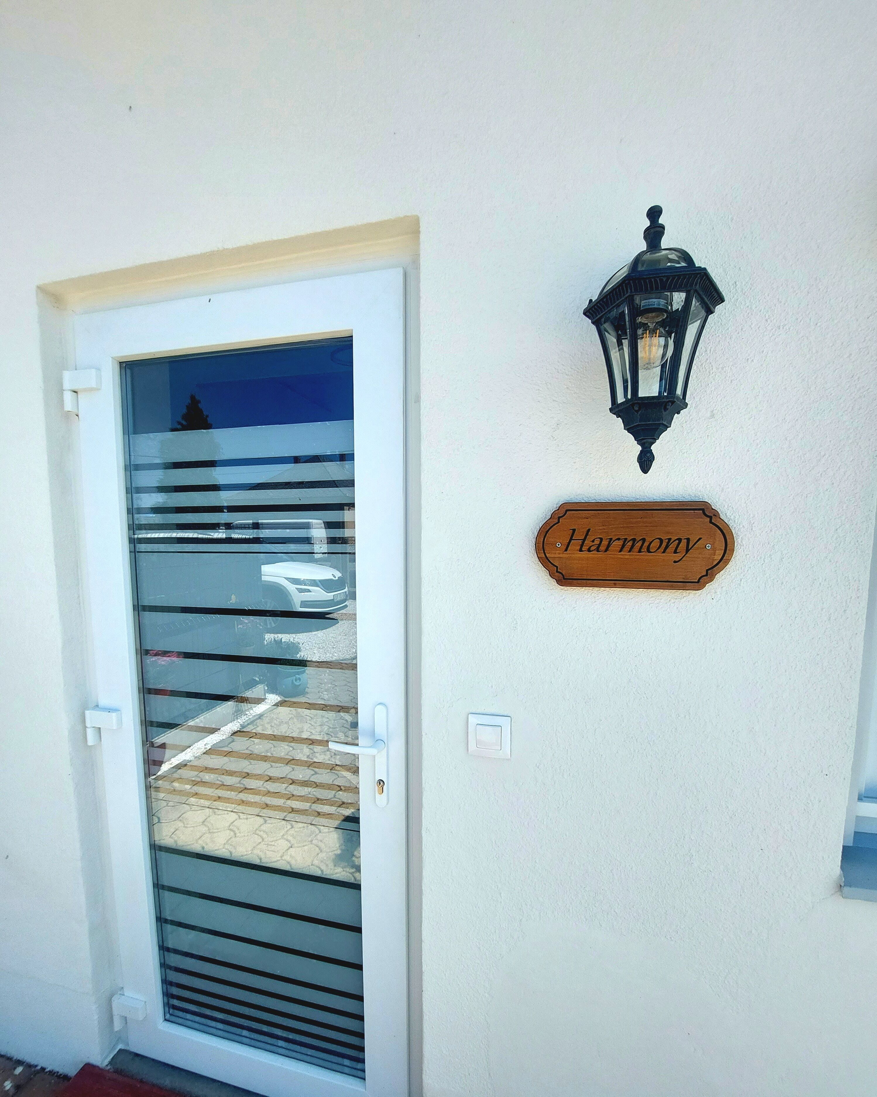 Una puerta con un panel de vidrio y una señal de madera que dice "Harmony" en la pared de al lado.