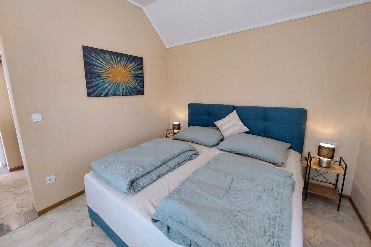A bedroom with a bed, a nightstand, a lamp, and a wall painting.