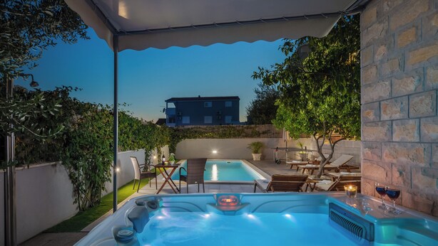 Ein Whirlpool mit Tisch und Stühlen, ein Schwimmbecken und ein Gebäude im Hintergrund.