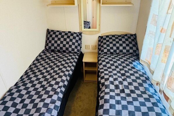 Una habitación con dos camas individuales, cada una con una colcha a cuadros, una mesita de noche pequeña y un espejo sobre la cama.