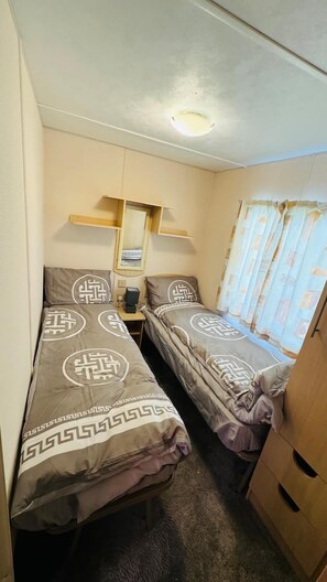A compact room with two beds, a small table, a mirror, and a window with curtains.