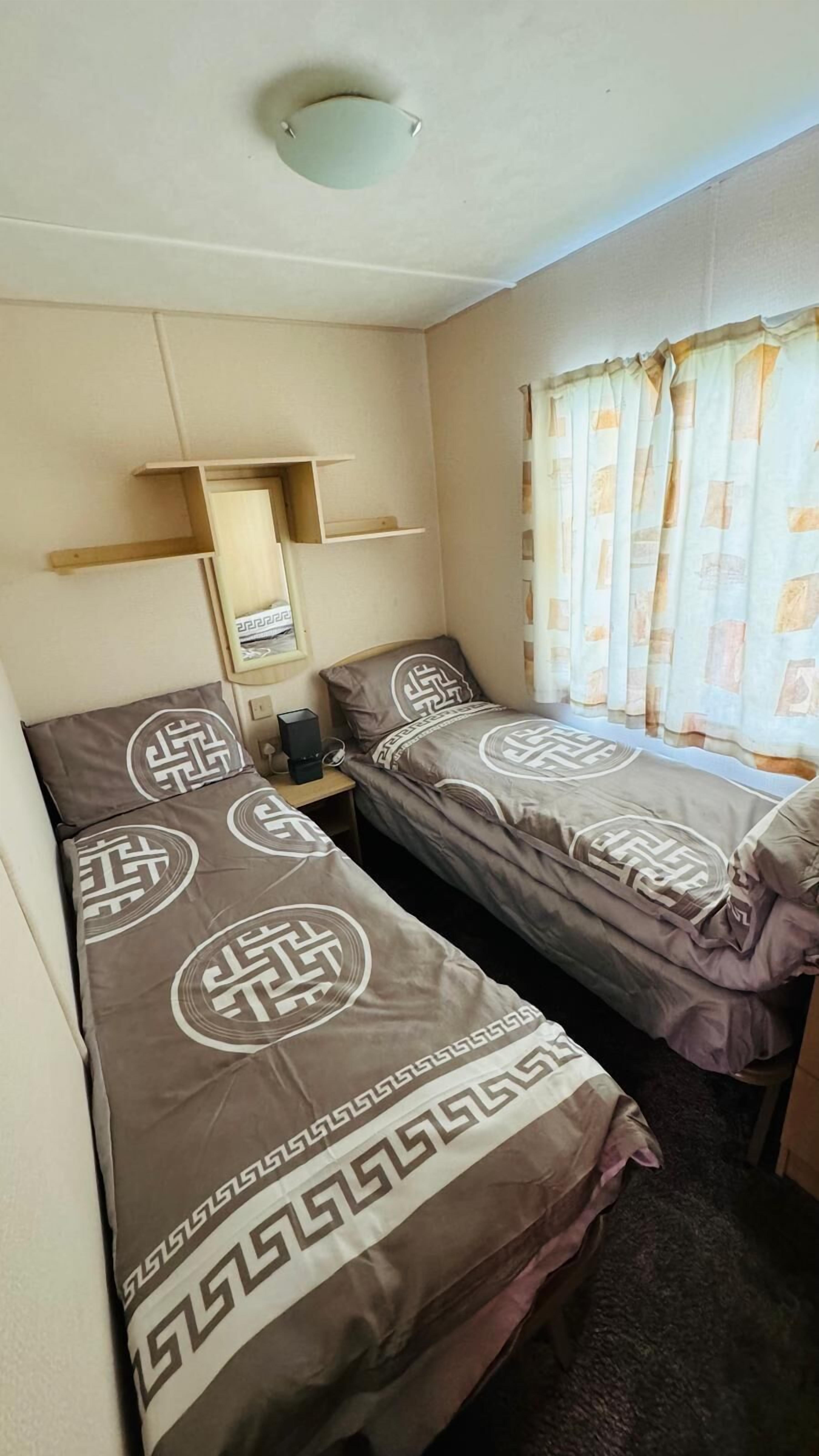 A room with two beds, a shelf, a mirror, and a window with curtains.