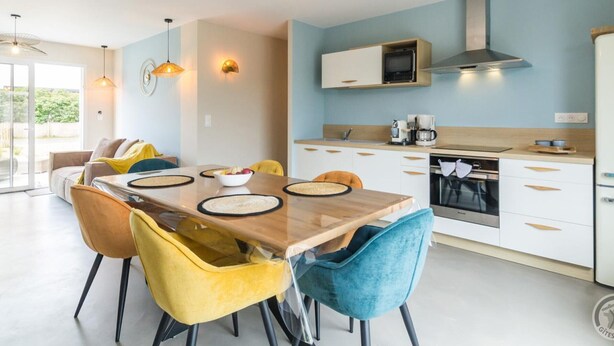 A modern kitchen with white cabinets, a microwave, and a stove. There is a dining area with a wooden table and chairs. - Charming Modern Bungalow with Nordic Hot Tub, Near Beach and Amenities in Saint-Jean-de-la-Rivière (Saint-Jean-de-la-Rivière)