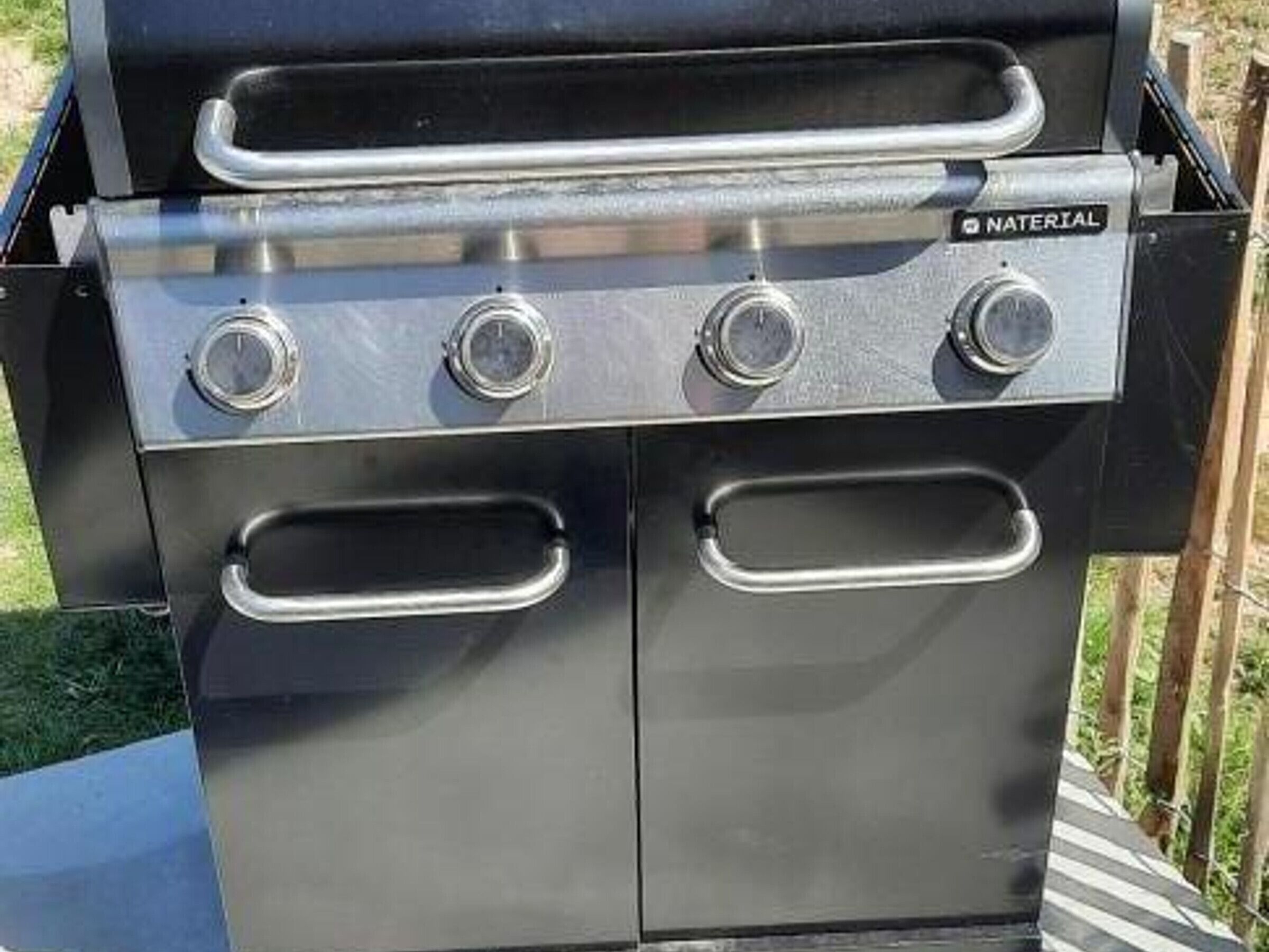 A black barbecue grill with four control knobs and two side handles.