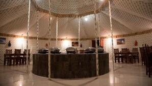 Une pièce circulaire dotée d’un plafond orné de motifs, d’une table centrale en pierre et de chaises en bois disposées autour.