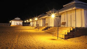 Une rangée de tentes, chacune dotée de quelques marches menant à l’entrée et éclairée par une seule lampe.
