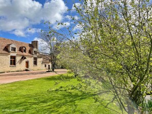 A stone building with a tiled roof, a paved driveway, and a grassy lawn.