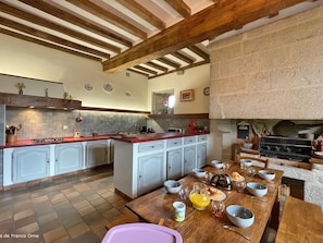 Una cocina amplia con una isla central, vigas de madera en el techo y una chimenea de piedra.