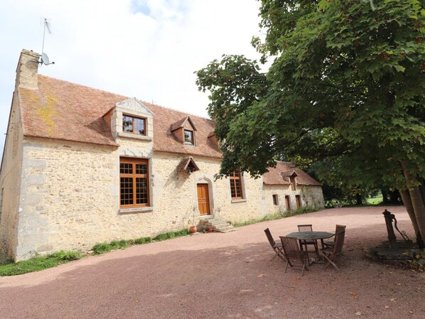 A stone building with a tiled roof, a wooden door, and a small porch area.