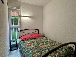 Cozy retreat with a single bed, nightstand, and a window offering a view of lush greenery.