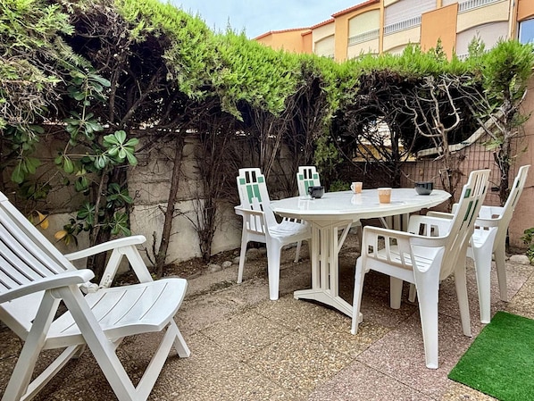 Enjoy a patio with a round table and six chairs, surrounded by lush greenery and a low stone wall.