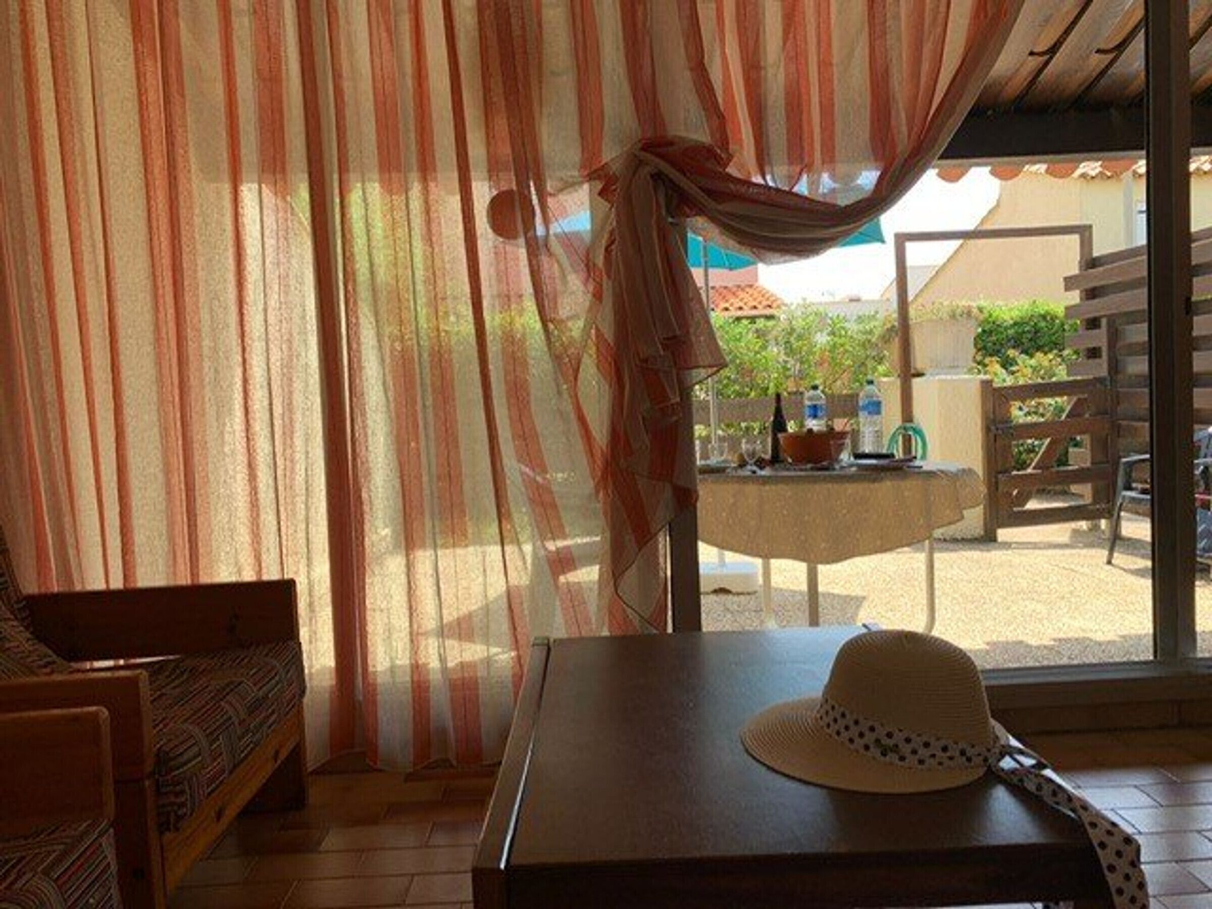 A room with a wooden table, a hat, and a view of an outdoor area with a table and chairs.