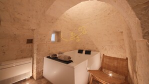 A stone-walled room with a white bathtub, a small window, and a wooden chair. - TD Trulli Benedetta w Pool in Peaceful Nature (Castellana Grotte)
