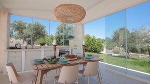 A modern kitchen with large windows, a dining table set for four, and a view of the outdoors. - TD Trulli Benedetta w Pool in Peaceful Nature (Castellana Grotte)