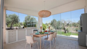 A modern kitchen with large windows, a dining table set with plates and bowls, and a hanging light fixture. - TD Trulli Benedetta w Pool in Peaceful Nature (Castellana Grotte)