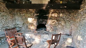 A stone-walled room with a fireplace, two wooden chairs, and a grill. - Natuurhuis (Orliac)