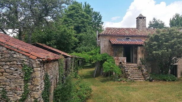 A rustic stone building with a tiled roof, surrounded by lush greenery and trees. - Natuurhuis (Orliac)