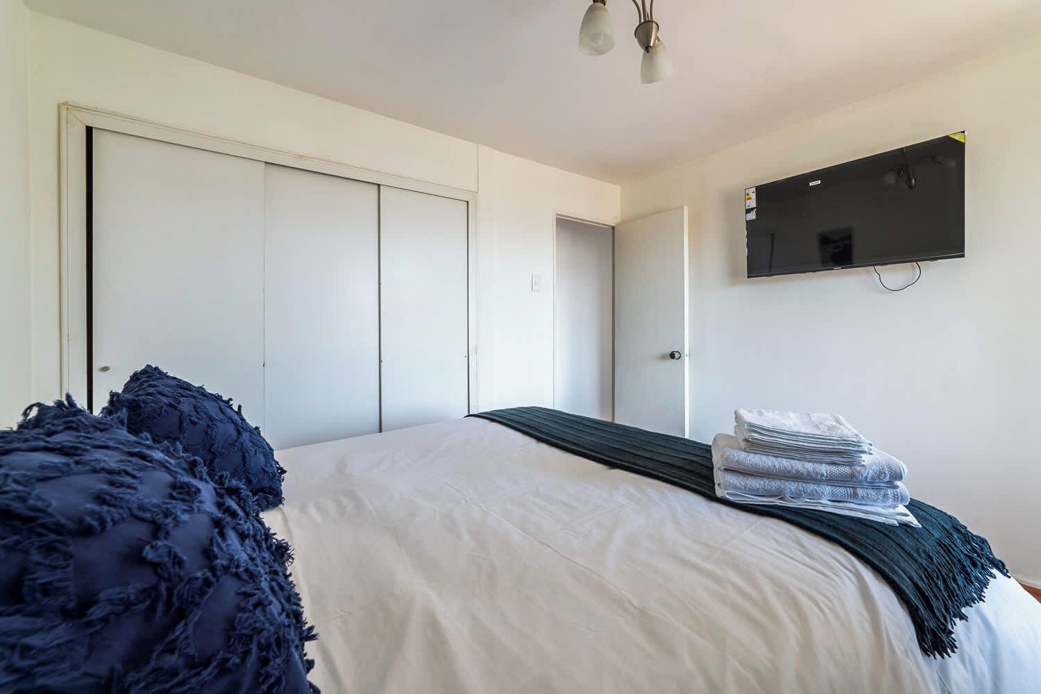 Een slaapkamer met een bed, een aan de muur bevestigde televisie en een deur naar een andere kamer.