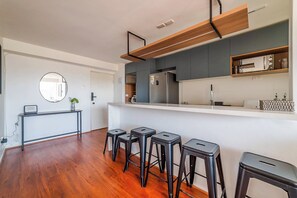 A modern kitchen with a built-in oven, a microwave, and a coffee machine. There are four black stools arranged in front of the counter.