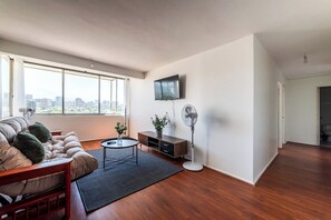 A modern living room with a sofa, a coffee table, a TV, and a standing fan.