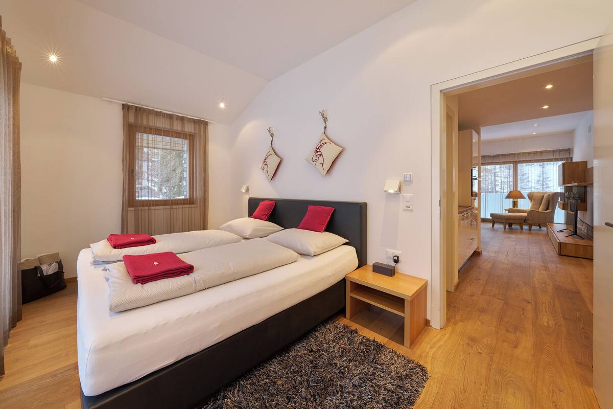 A modern bedroom with a large bed, a nightstand, and a view of the living area.
