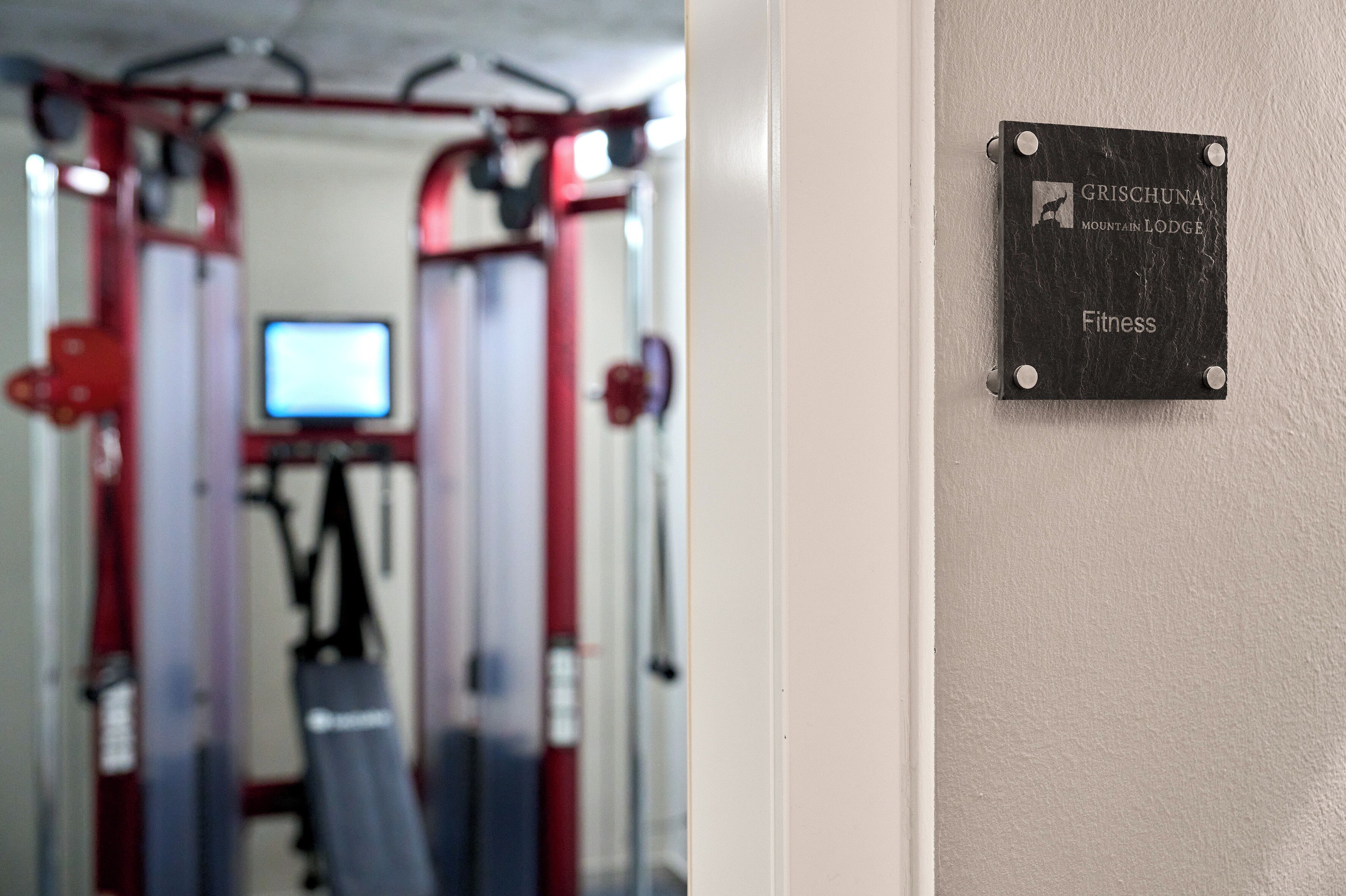 Ginásio com equipamentos de exercício e um aviso indicando que pertence ao Fitness da Pousada Grishchuna Mountain Lodge.
