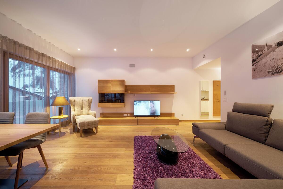 A modern living room with a wooden floor, a sofa, a dining table, and a TV.