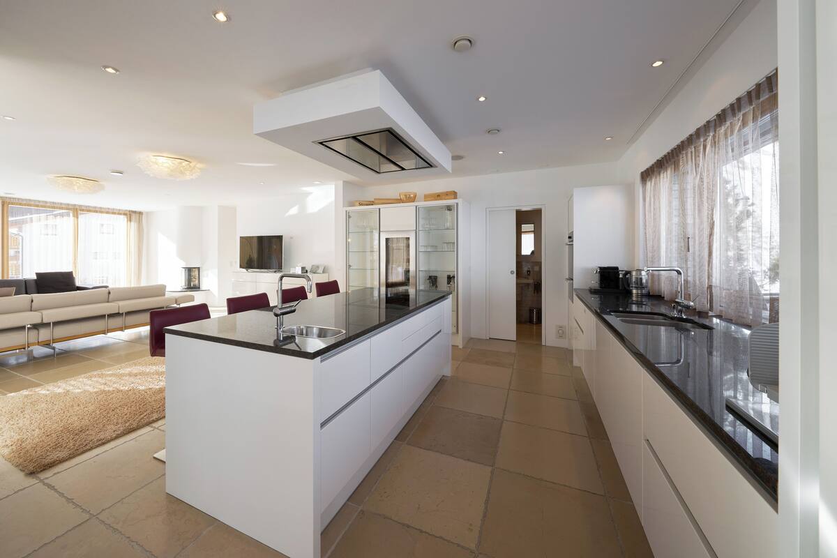 A modern kitchen with a central island, a dining area with a sofa and chairs, and a living room with a TV and a fireplace.