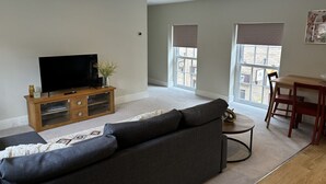 Ein Wohnzimmer mit Sofa, Fernseher, Holz-Multimedienmöbel, Esstisch und Stühlen.
