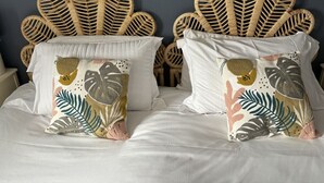 Ein Bett mit einem Kopfteil aus gewobenem Rattan, zwei Kissen mit tropischem Blattmuster und einer schlichten weißen Bettdecke.
