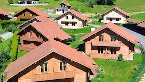 Un ensemble de chalets en bois aux toits en pente, entourés de prairies verdoyantes et d’arbres.