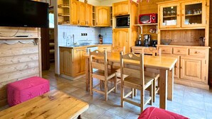 A cozy kitchen with wooden cabinets, a dining table, and a television mounted on the wall.