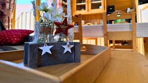 A rustic wooden table with a decorative centerpiece featuring white flowers and red stars, set against a window with curtains.