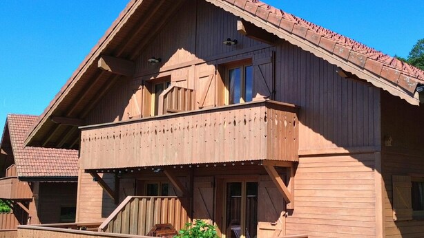 A wooden house with a balcony, a wooden deck, and a small garden area.