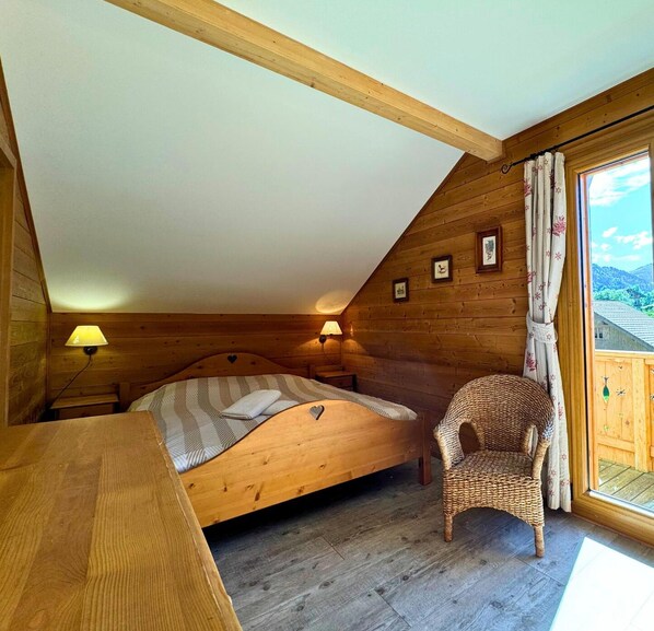 Cozy retreat with a wooden bed, bedside lamps, and a wicker chair, offering a view of the surrounding greenery.