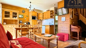 Une cuisine chaleureuse avec des meubles en bois, une table à manger et des chaises. Il y a une horloge au mur et un téléviseur sur le côté droit.