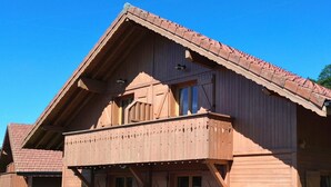 Une maison en bois dotée d’un balcon, d’une terrasse en bois et d’un petit jardin.