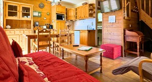 Une cuisine chaleureuse avec des meubles en bois, une table à manger et des chaises. Il y a une horloge au mur et un téléviseur sur le côté droit.