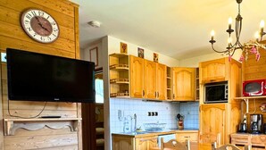 A cozy kitchen with wooden cabinets, a dining table, and a television mounted on the wall. - Z-Chalet Mitoyen 6A., Z-Chalet Mitoyen 6A. (Mont-Saxonnex)