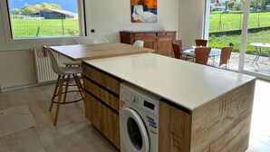 A modern kitchen with a central island, a built-in washing machine, and a large window offering a view of a green field. - Beautiful villa with mountain view, Beautiful villa with mountain view (Châteauneuf)